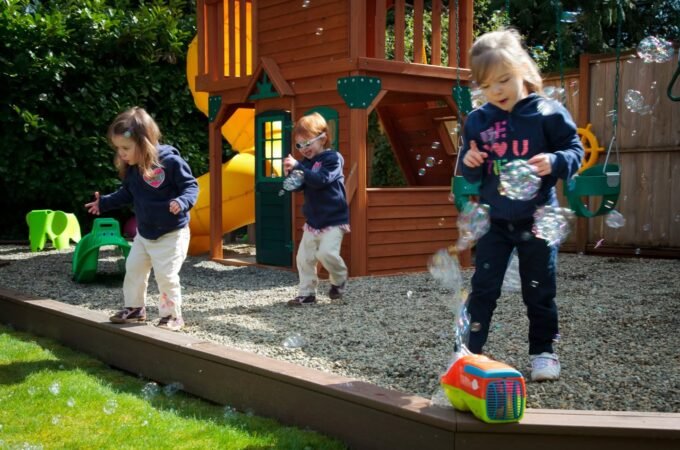 Children playing with bubbles in a backyard featuring a wooden playset.