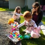 Children collecting colorful plastic eggs near a green slide while an adult watches nearby.