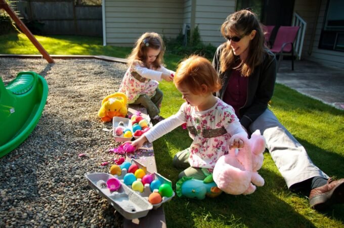 Children collecting colorful plastic eggs near a green slide while an adult watches nearby.