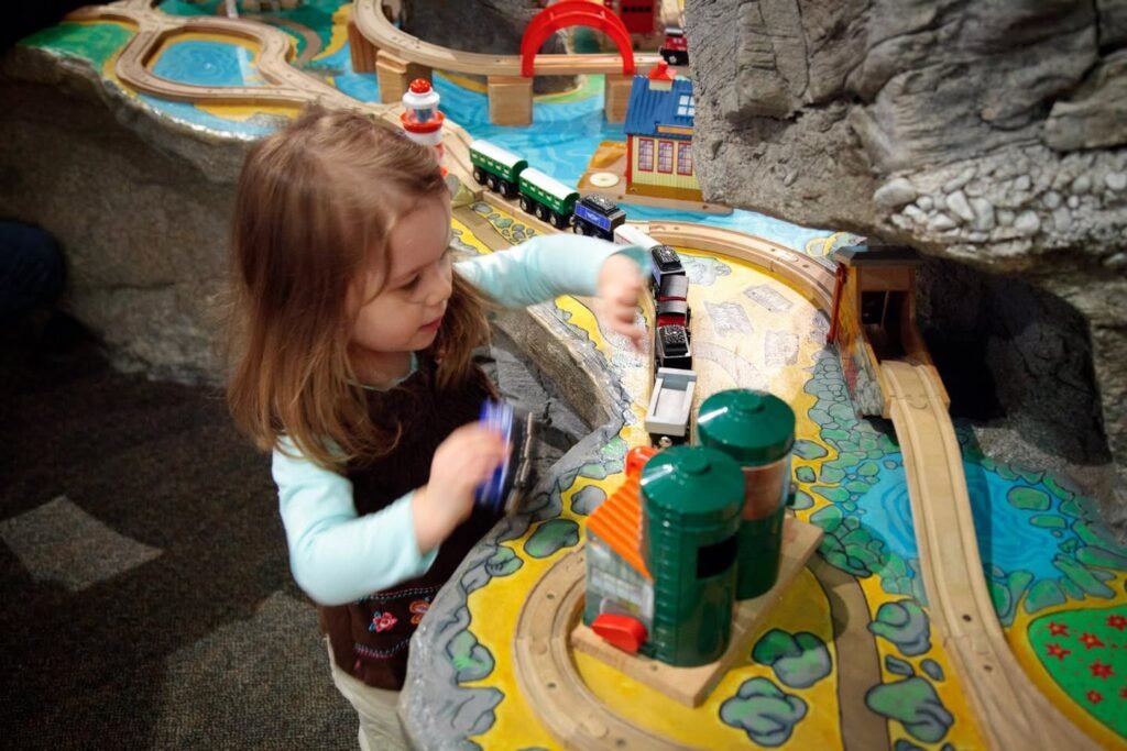 A child plays with a colorful wooden train set at an indoor exhibit.