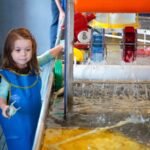 A child playing with water at an interactive exhibit featuring colorful pipes and flowing water.