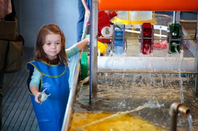 A child playing with water at an interactive exhibit featuring colorful pipes and flowing water.