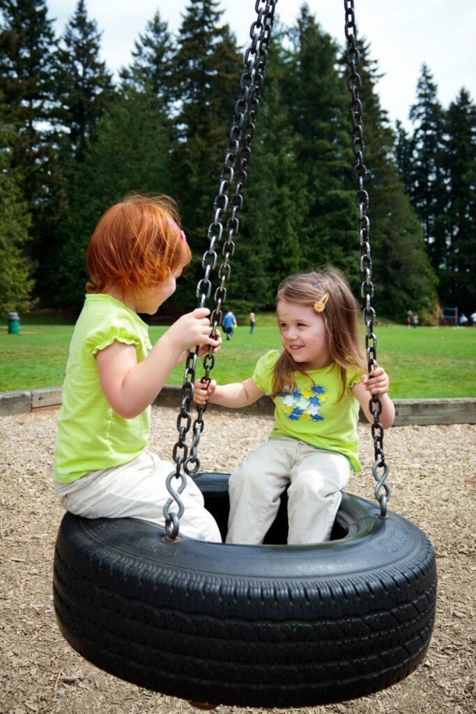 Children enjoying a tire swing in a lush Pacific Northwest park with tall evergreens in the background.