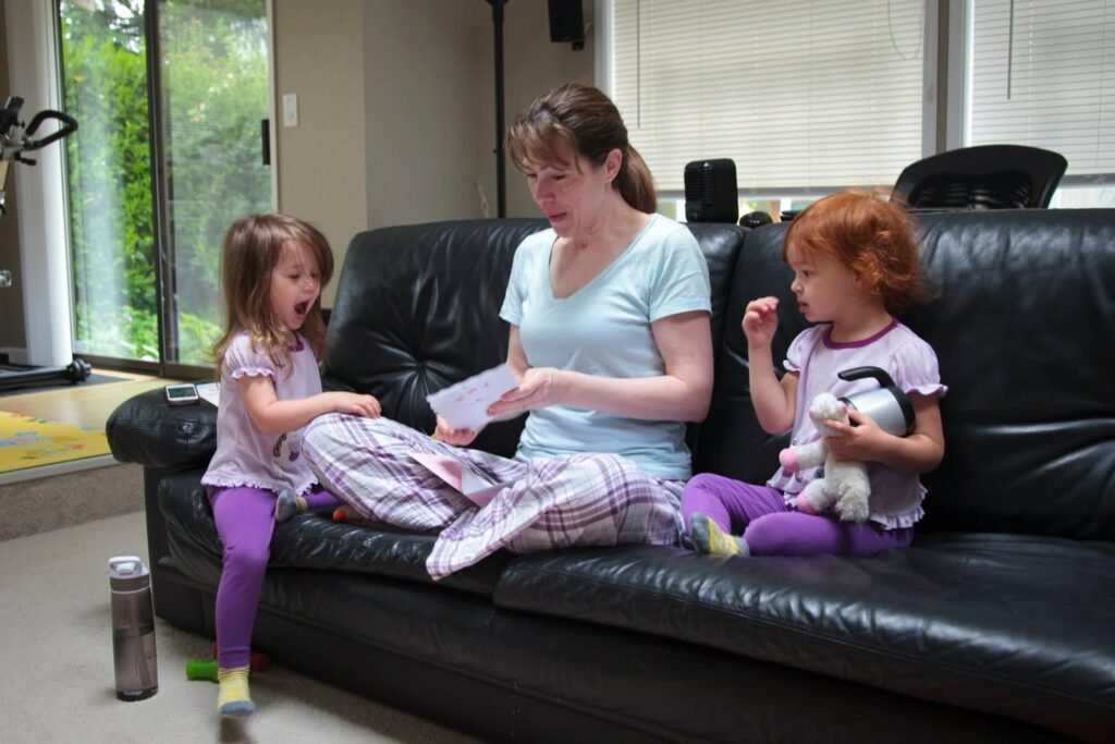 A comfortable indoor scene showing a woman and two children relaxing together on a large black leather sofa.