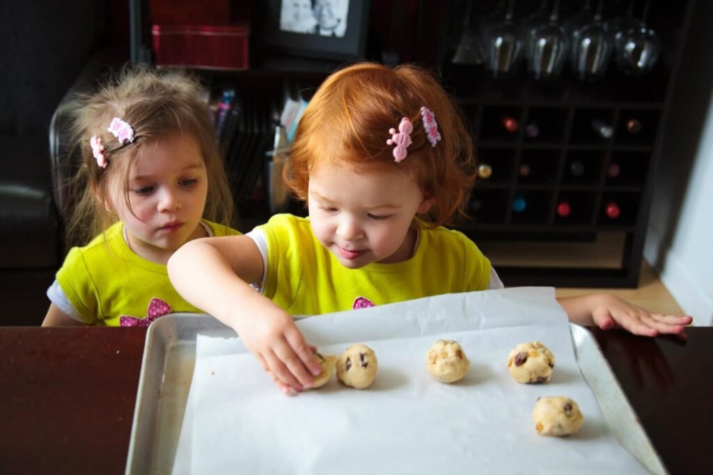 Two children in matching yellow shirts preparing cookie dough on a baking sheet.