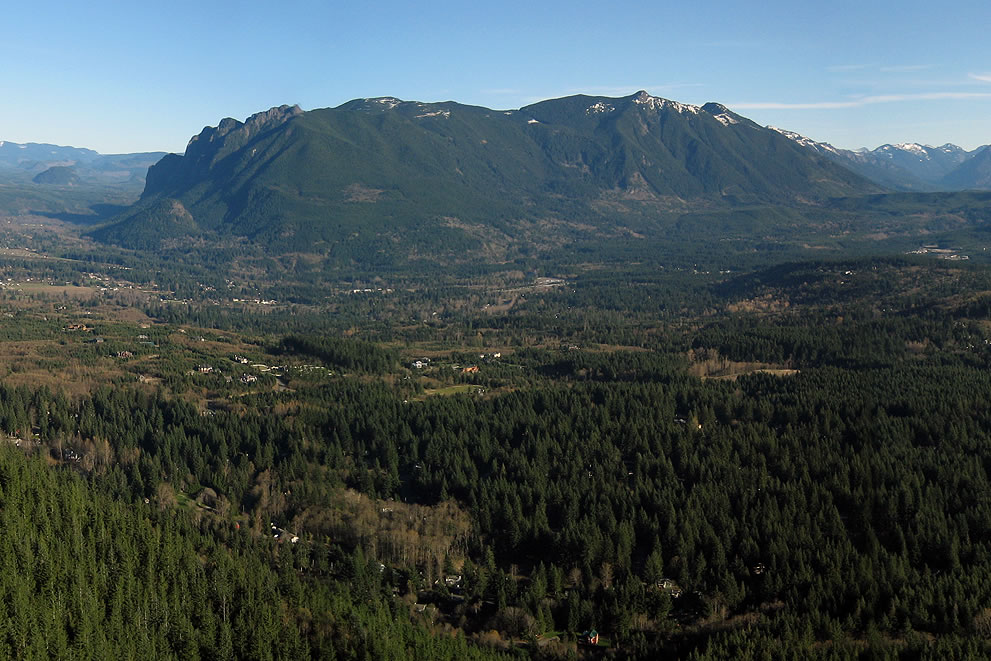 A scenic view of lush green forests and rugged mountains under a clear blue sky in the Pacific Northwest.
