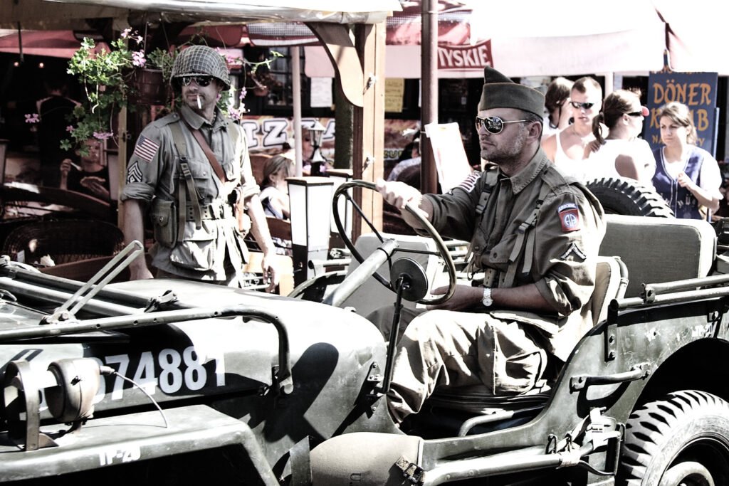A vintage jeep numbered 74881 is parked in a bustling outdoor market, with people dressed in various attire milling about in the background.