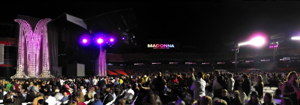 A vibrant nighttime concert scene at the Cau Ferrat Festival in Sitges, Spain, with a large illuminated stage structure and purple lighting.