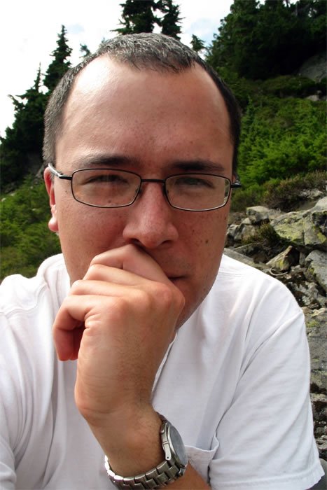 John rests his chin on his hand, surrounded by lush greenery and rocks in the Pacific Northwest.