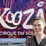 U2 at The Rose Bowl A woman stands smiling in front of a vibrant KooZA Rawhauh by Cirque du Soleil sign.