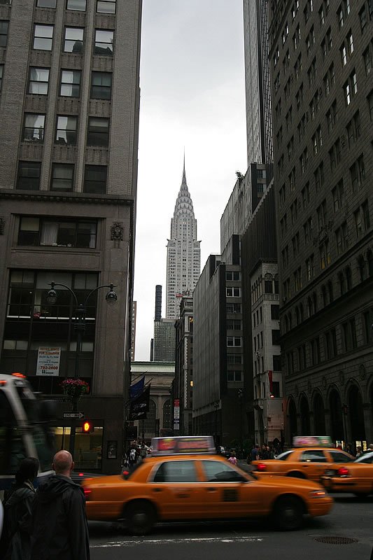A bustling street scene in New York City featuring yellow taxis and the iconic Chrysler Building in the background.
