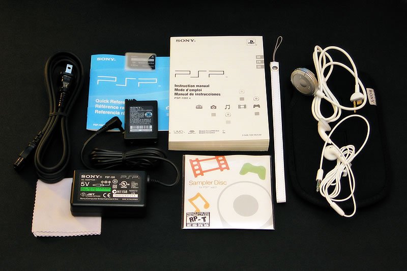 A collection of PSP accessories and manuals laid out on a black surface, including headphones, a USB cable, a battery pack, and instructional booklets.
