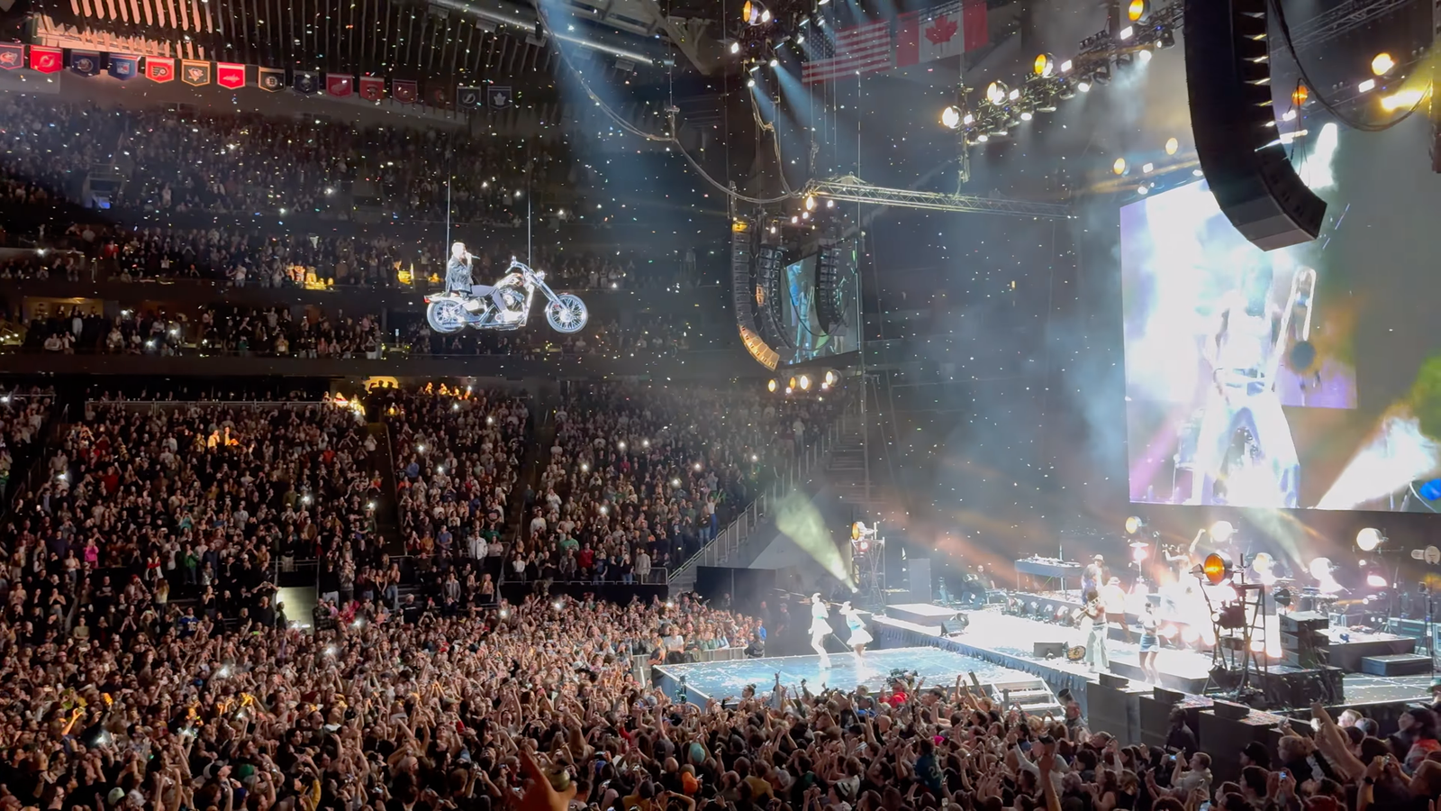Macklemore A performer executes a motorcycle stunt on a suspended track during an arena concert, captivating a packed audience.