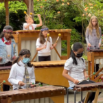 Students performing on a wooden carillon in an outdoor garden setting.