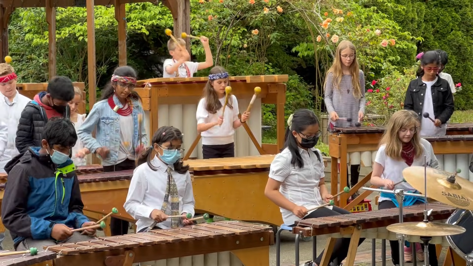Miranda’s Final Marimba Performance Students performing on a wooden carillon in an outdoor garden setting.