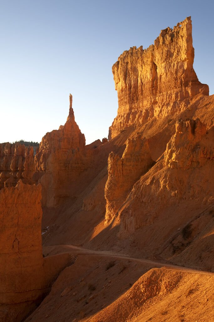 Golden light bathes the Zechstein Hills in Calgary, showcasing towering sandstone formations and a winding path.