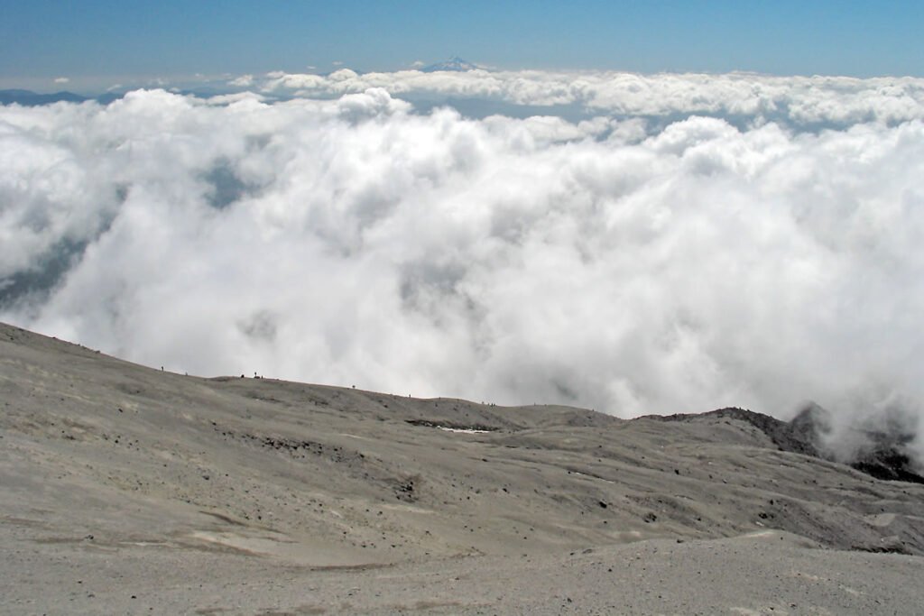 A breathtaking view of a mountain peak towering above a sea of fluffy white clouds under a clear blue sky.