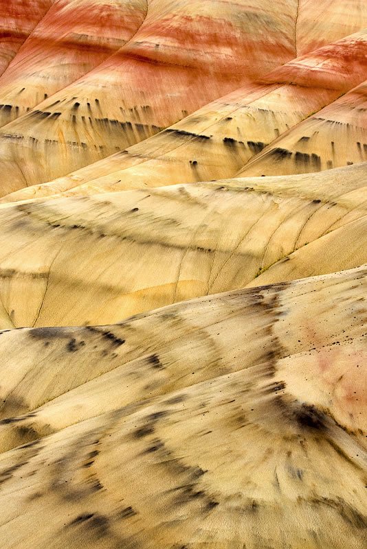 Abstract desert rock formation showing layered patterns in sandstone hues of tan and red. A dynamic interplay of textures creates a visually suggestive, almost fluid surface. Its subtle details evoke natural landscapes sculpted by time and weather.