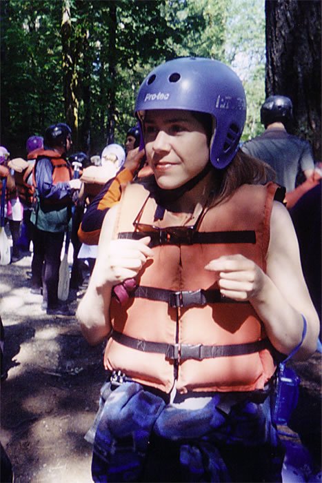 A person wearing a helmet and life vest, surrounded by trees. Group members are also equipped for an outdoor adventure.