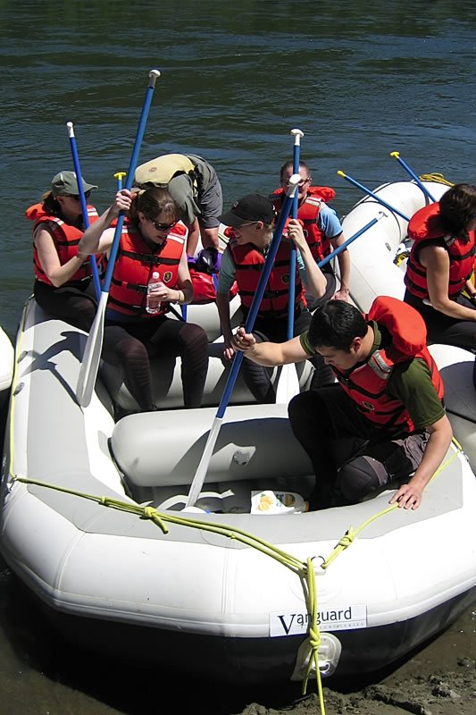 Several people wearing life jackets are seated in a white inflatable raft on calm water, engaging in a recreational boating activity.