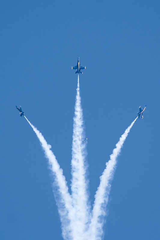 Three airplanes flying in formation leaving white smoke trails against a clear blue sky.