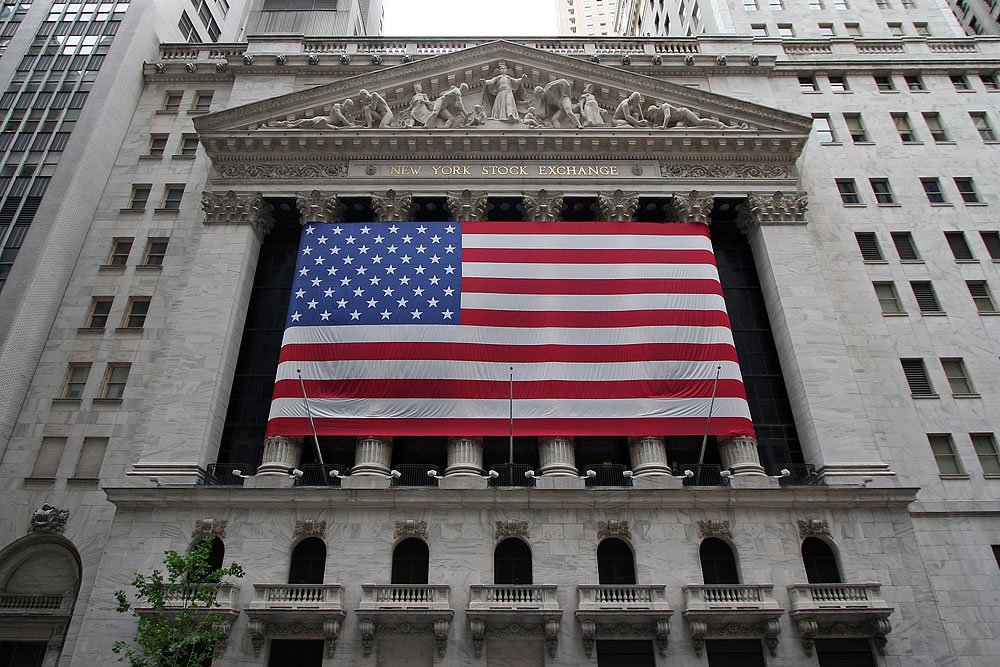 A large American flag displayed prominently on a classical-style building in a cityscape