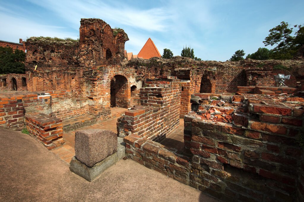 The image shows ancient brick ruins with arches and walls, set against a clear blue sky. The structure appears to be part of an old historical site, possibly a temple or fortress.