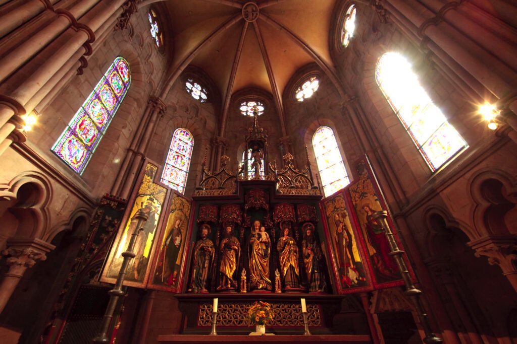 A detailed view of an intricately designed altar with statues, surrounded by arches and illuminated by colorful stained glass windows.