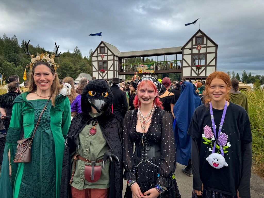 A group of friends posing in medieval costumes at a Renaissance fair with a Tudor-style building in the background.