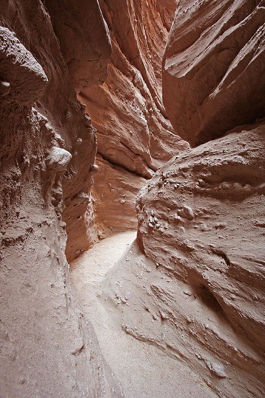 A narrow, winding slot canyon with smooth, undulating sandstone walls showcasing natural erosion patterns in warm hues.