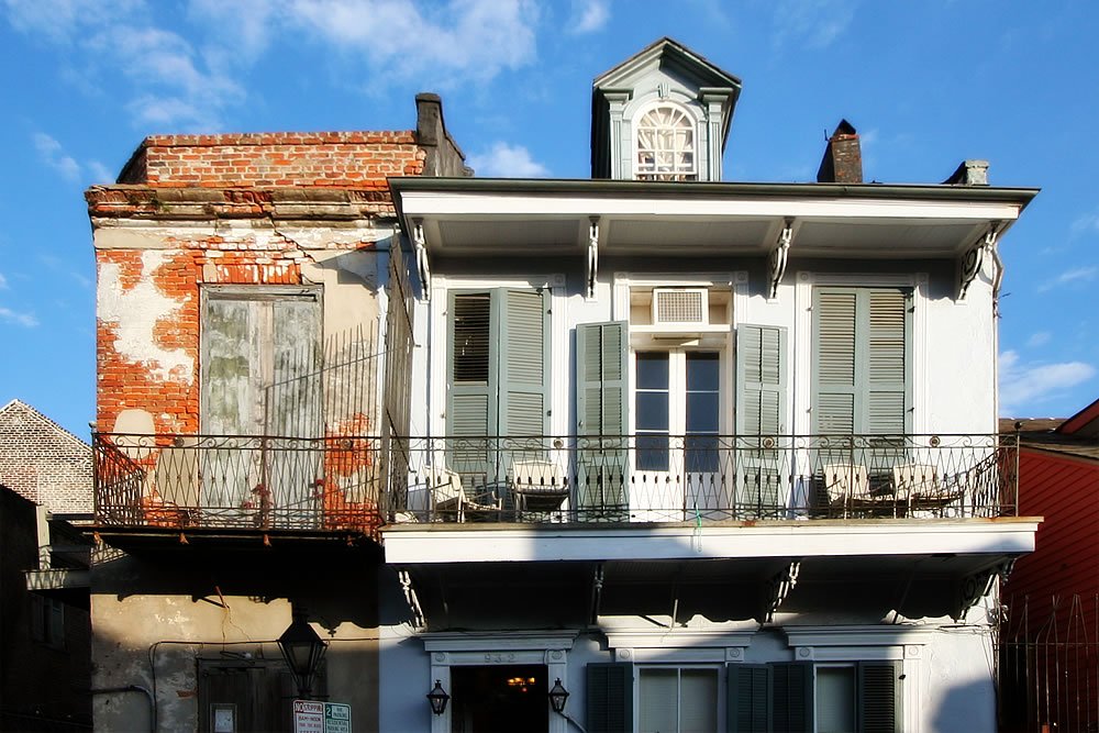 A beautifully weathered antique house in the Pacific Northwest, featuring a charming clock tower, white wooden façade, and a balcony adorned with chairs overlooking the street.