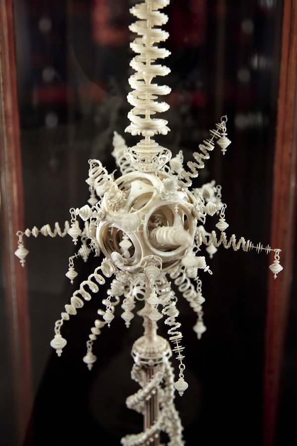 An antique-style chandelier with intricate white details and dangling ornaments, reflecting on a dark surface.