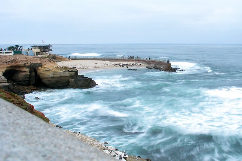 La Jolla A lively street lined with trees and people enjoying their time sitting on benches and walking around.