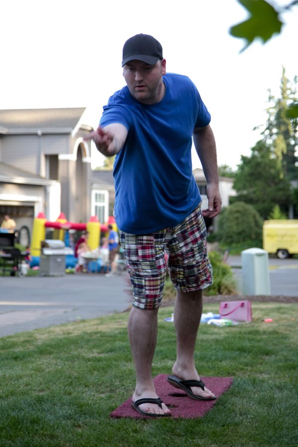 A man in a blue shirt and plaid shorts is playing a game outside on the grass.