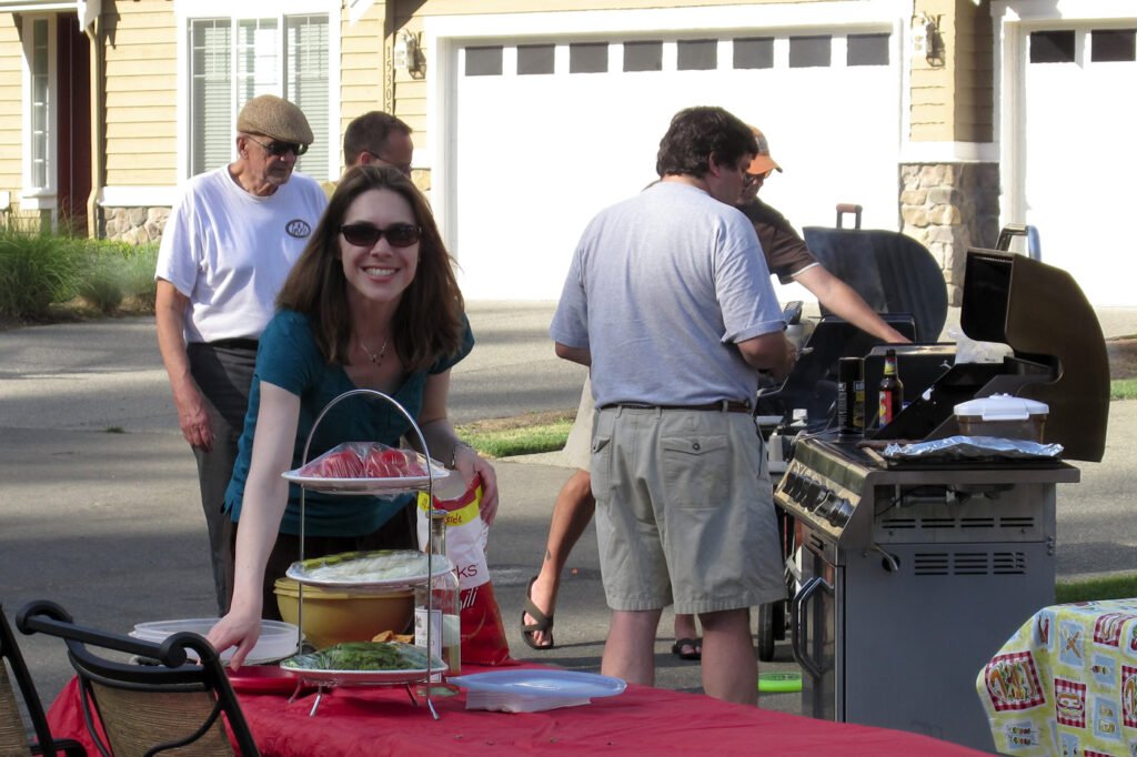 People enjoying a barbecue in a suburban backyard with food and drinks on a table.