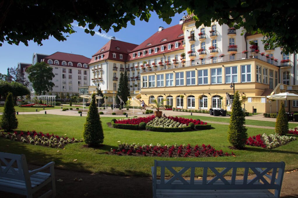 A picturesque garden with vibrant flower beds and benches, set against the backdrop of an elegant hotel building.