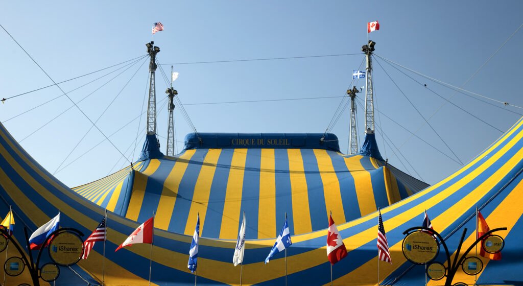 A vibrant blue and yellow striped circus tent adorned with international flags under a clear sky.