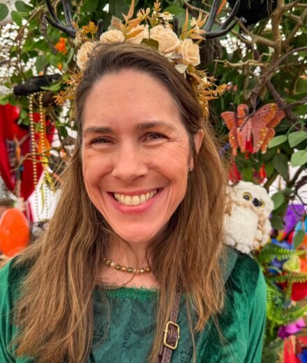 Woman wearing a flower crown at an outdoor market with festive decorations.