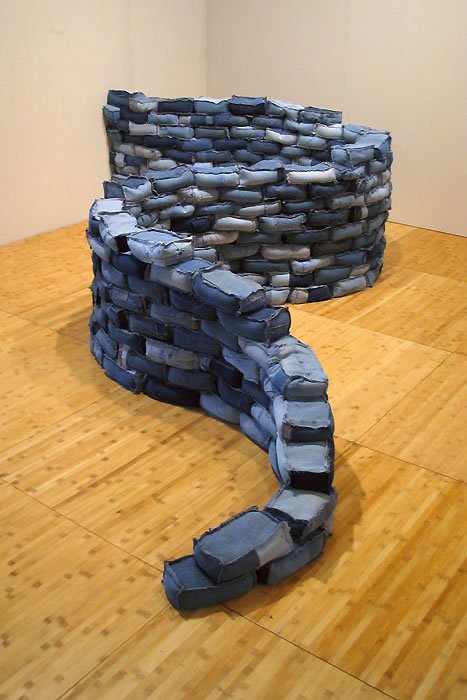 A detailed view of a sculpture made from blue and gray painted stones, crafted into a tiered, stepped structure sitting on a wooden floor.