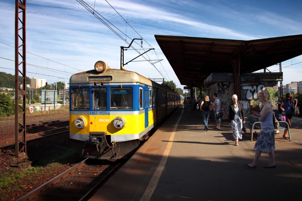 A bright blue and yellow train arriving at a station with passengers waiting on the platform.