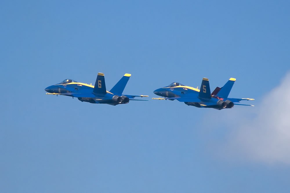 Four Blue Angels jets flying in tight formation against a clear blue sky.