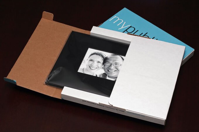 The image shows a couple from a personality photo, placed inside a brown paper bag alongside a white book and a blue booklet advertising 'mypub', captured from a top-down perspective. This arrangement suggests a cozy review or story-telling setting.