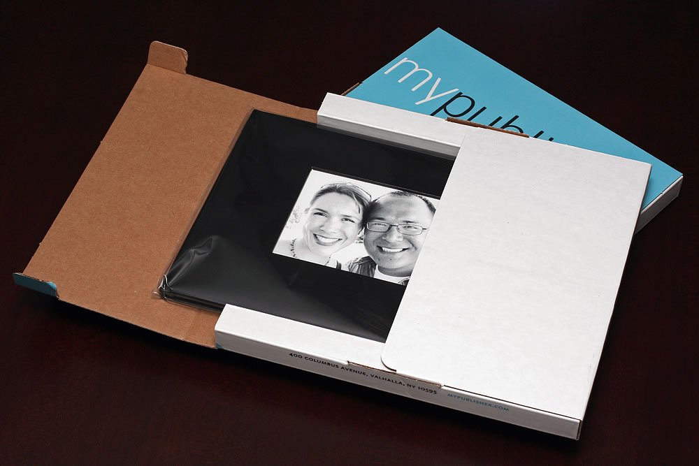 The image shows a couple from a personality photo, placed inside a brown paper bag alongside a white book and a blue booklet advertising 'mypub', captured from a top-down perspective. This arrangement suggests a cozy review or story-telling setting.