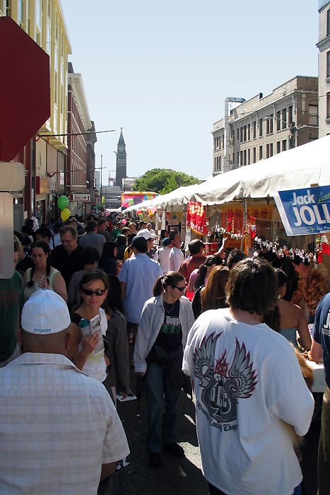 A busy street fair filled with people walking under white tents. A sign for Jack in the Box and a Jack Jolly banner are visible.
