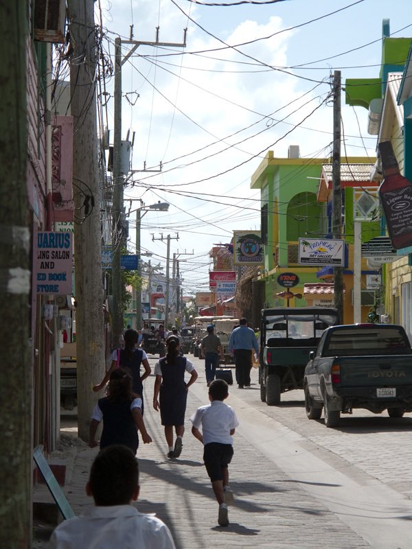 A bustling street scene featuring people walking and vehicles passing by, with colorful buildings and overhead wires.