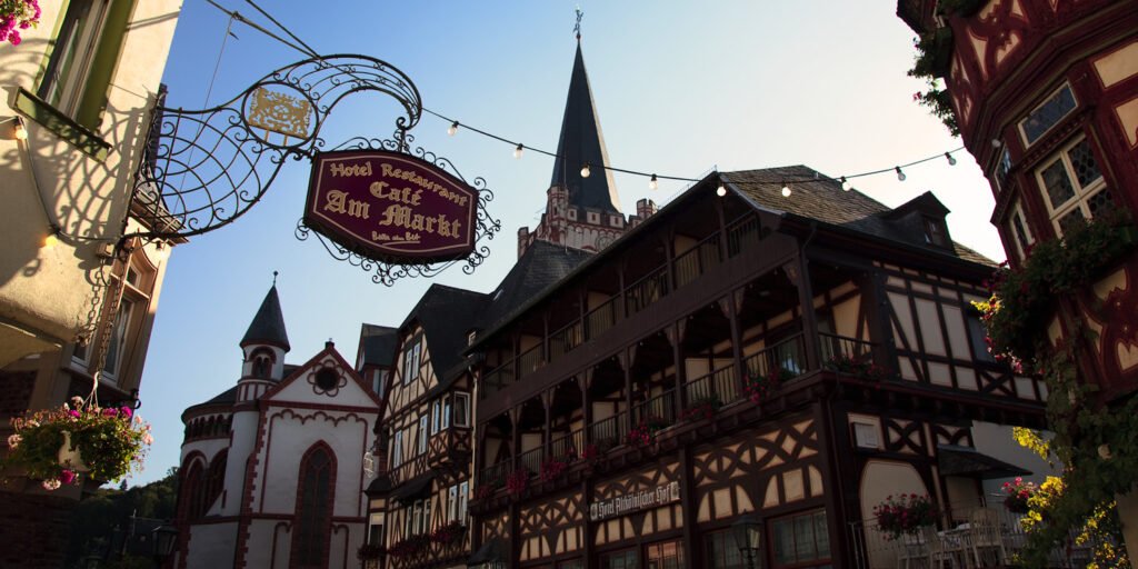 A picturesque view of Cafe Am Markt with half-timbered buildings and a church spire under a clear blue sky.