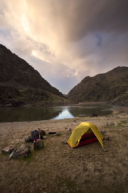 A yellow tent pitched by a lake with dramatic clouds above.