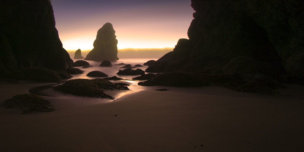 Silhouette of Haystack Rock at sunrise with smooth wet sand