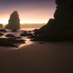 Mythbusters Silhouette of Haystack Rock at sunrise with smooth wet sand