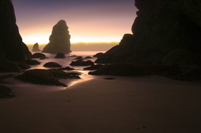 Silhouette of Haystack Rock at sunrise with smooth wet sand